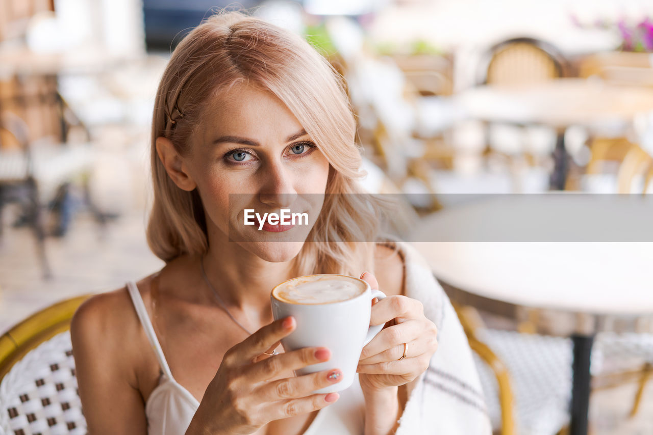 Portrait pretty blonde woman, smiling woman in cozy plaid, sitting in cafe