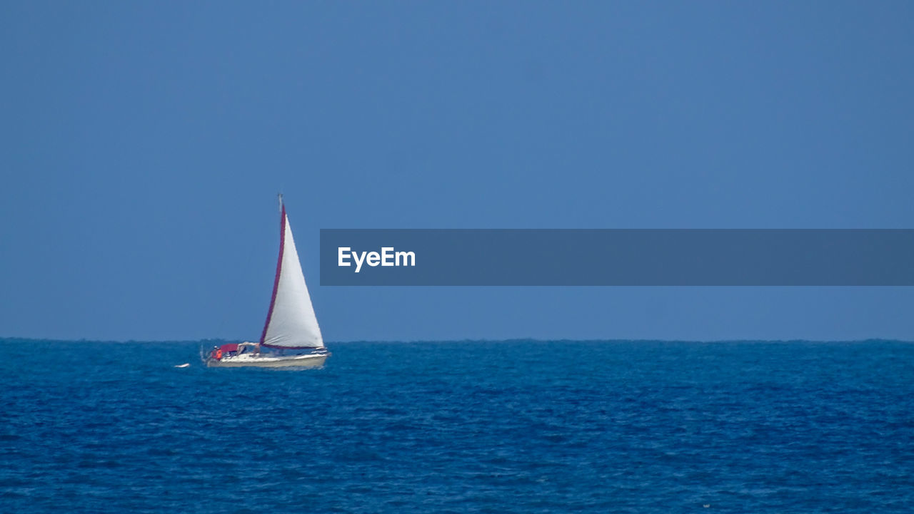 Sailboat sailing in sea against clear blue sky