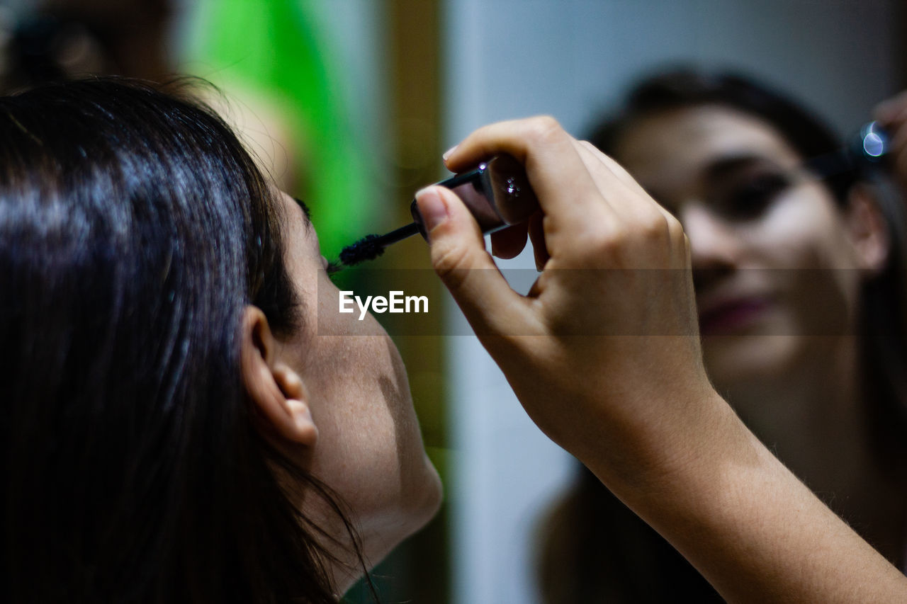 Close-up of woman applying mascara against mirror