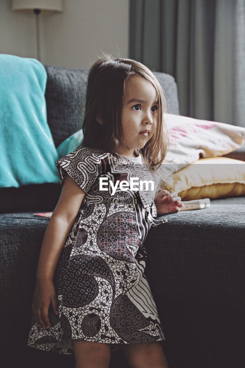 Girl looking away while standing by sofa at home