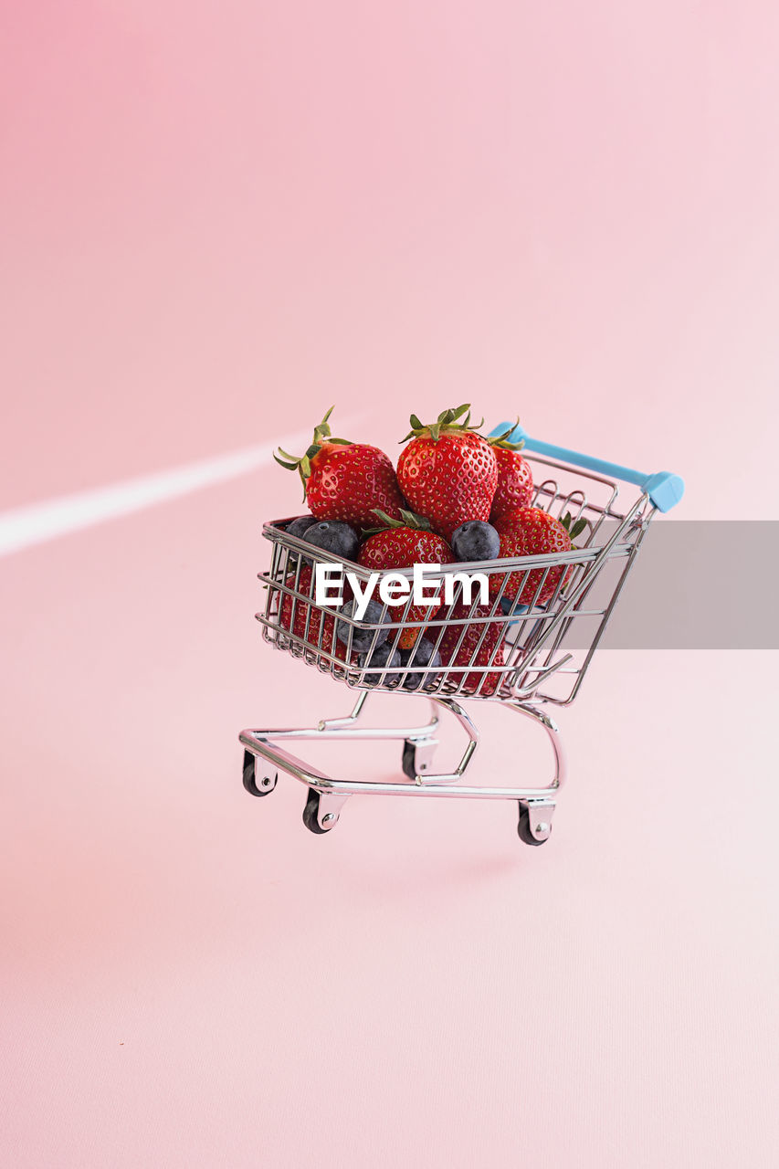 Close-up of strawberries and shopping cart over pink background