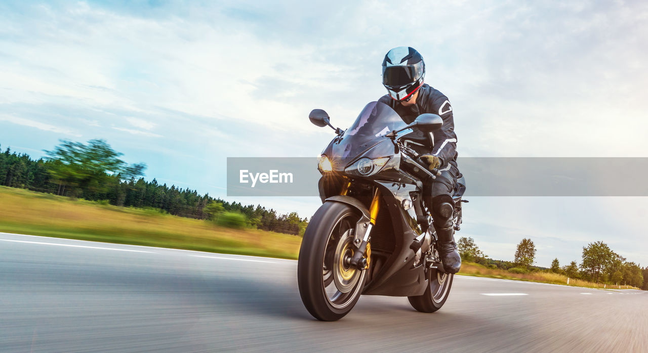 Man riding motorcycle on road against cloudy sky