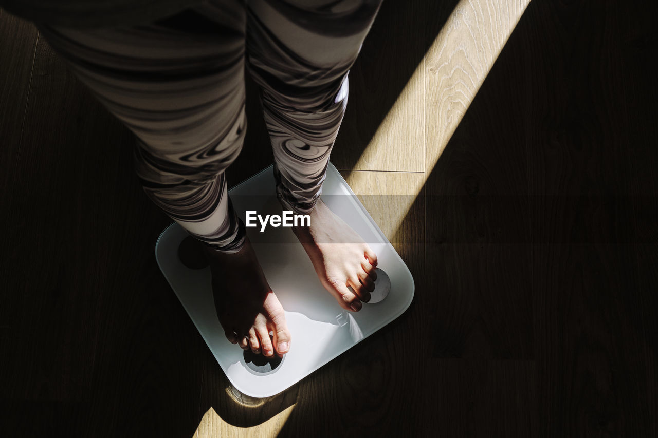 Young woman standing on weight scale in dark at home