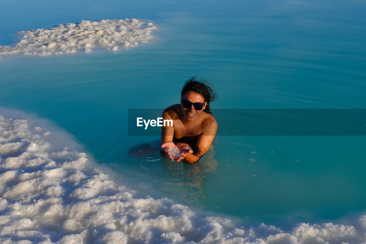A man in a blue salt water pond exfoliating the body.