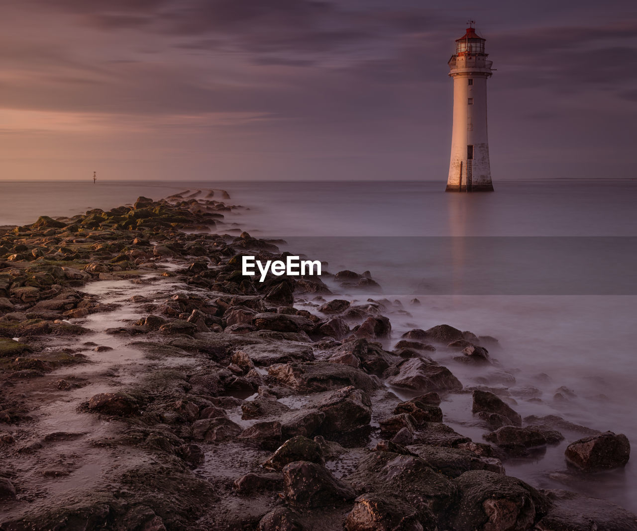 Lighthouse by sea against sky during sunset
