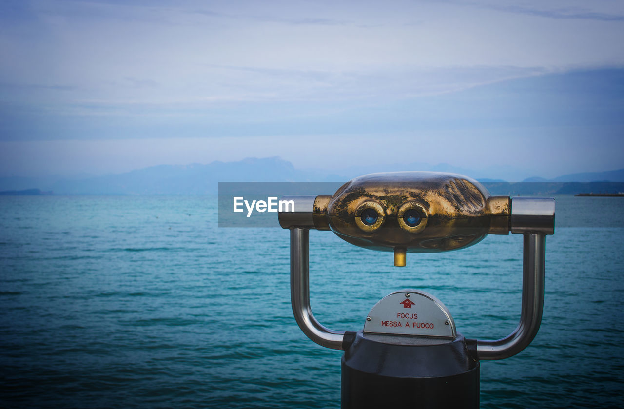 Coin-operated binoculars by sea against sky