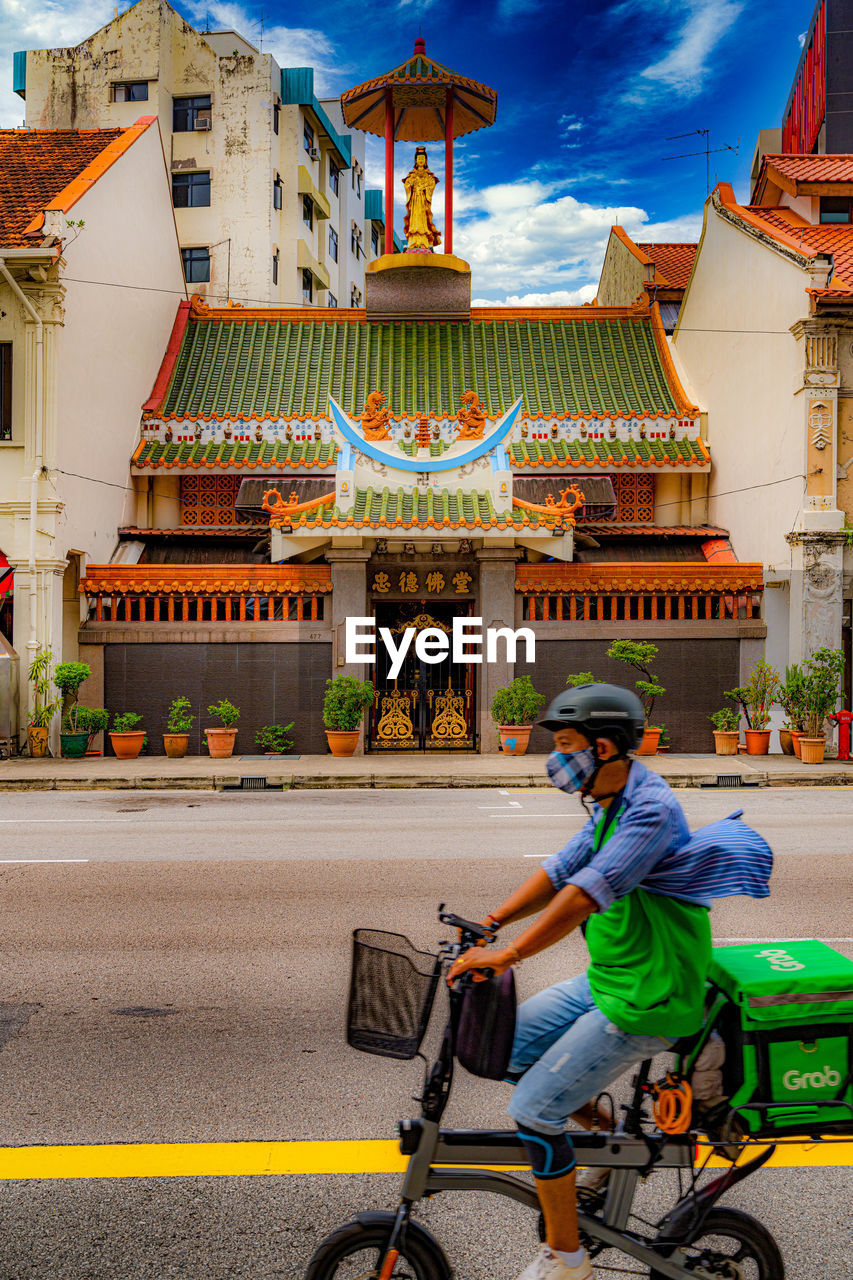 MAN RIDING BICYCLE ON STREET BY BUILDING