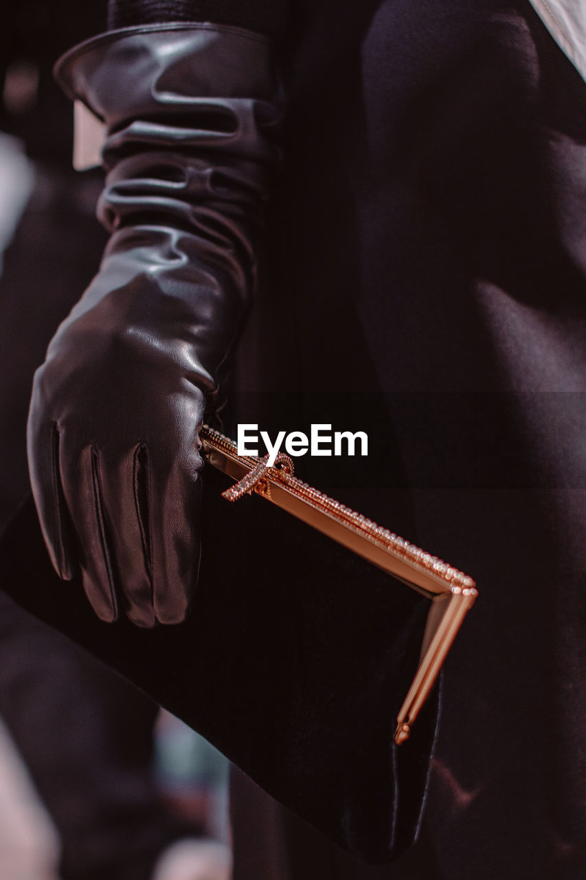 A female hand in a black leather glove holding a classic velvet clutch with a gold frame. 