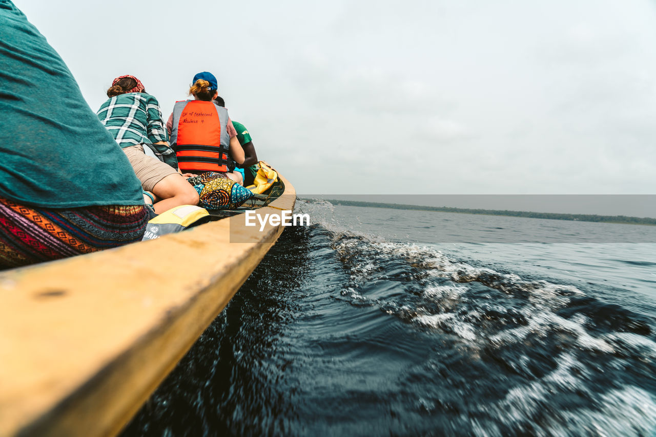 REAR VIEW OF MEN ON BOAT AGAINST SKY