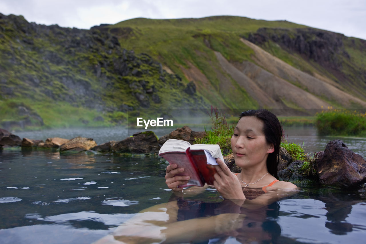 Woman reading book in thermal pool at landmannalaugar