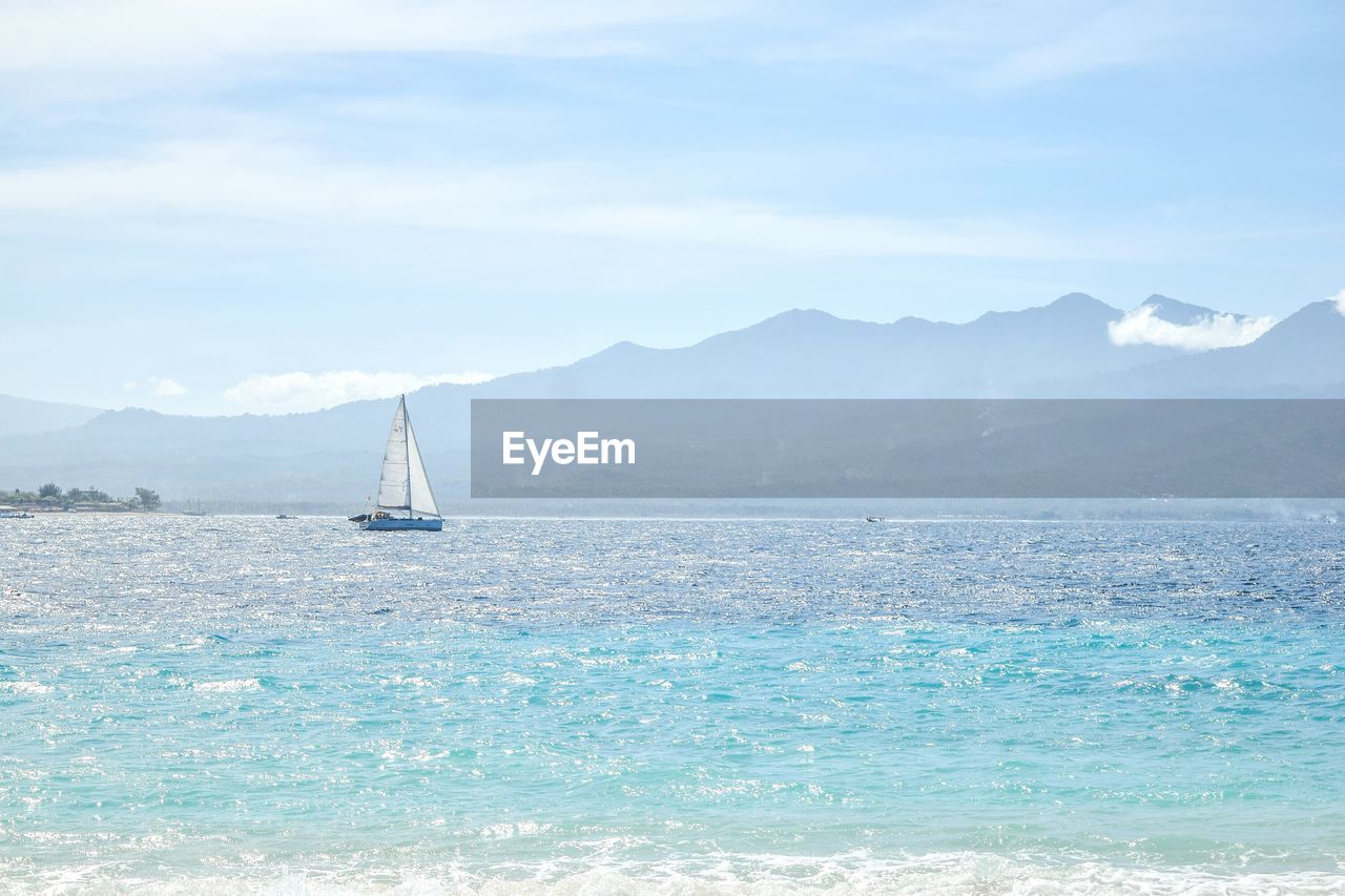 SAILBOAT SAILING ON SEA AGAINST MOUNTAINS