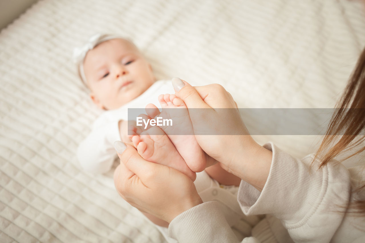 Mother massages her little daughter, newborn baby. lies on bed in bedroom, homely.