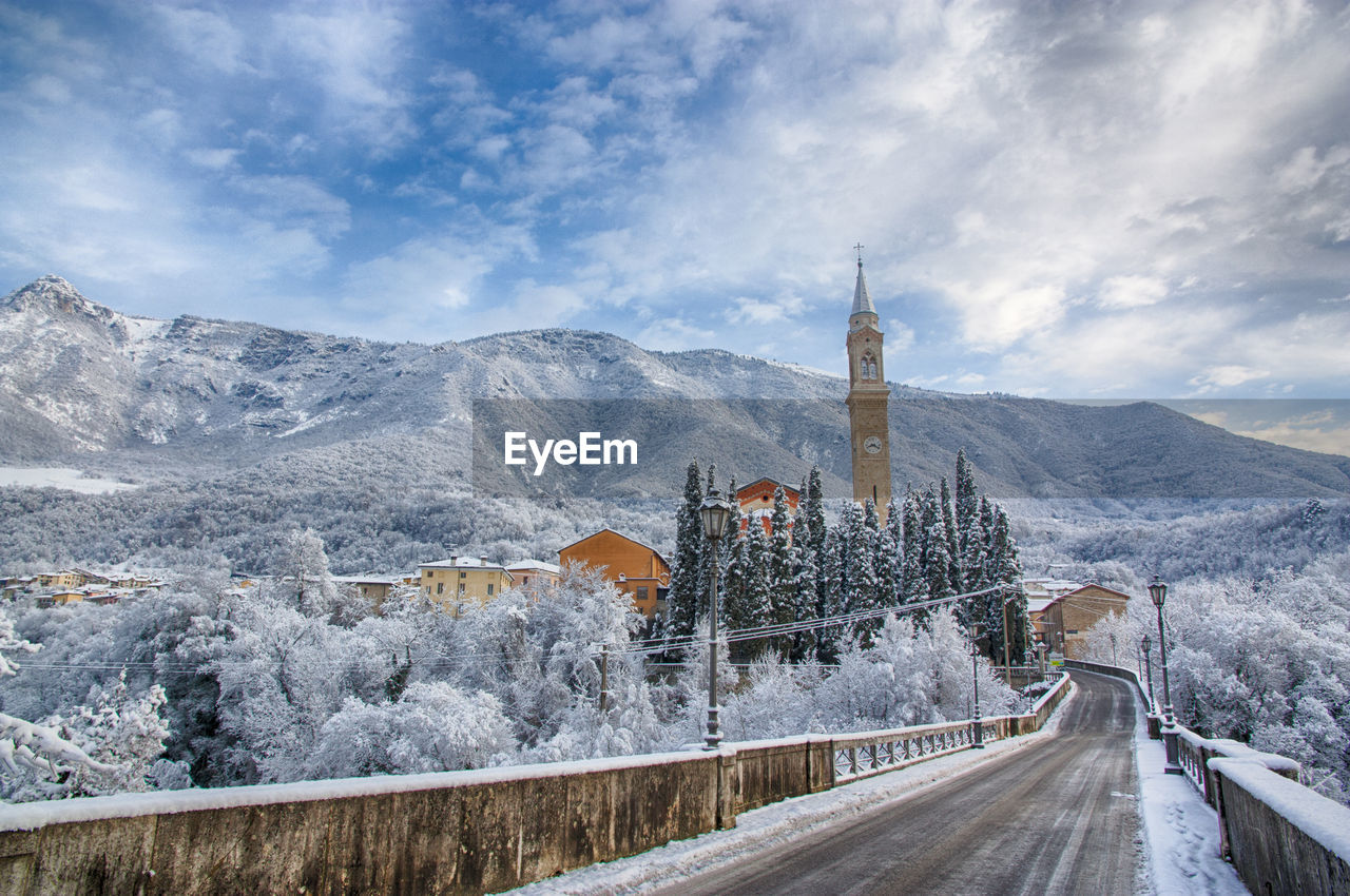 Road leading towards town against cloudy sky during winter