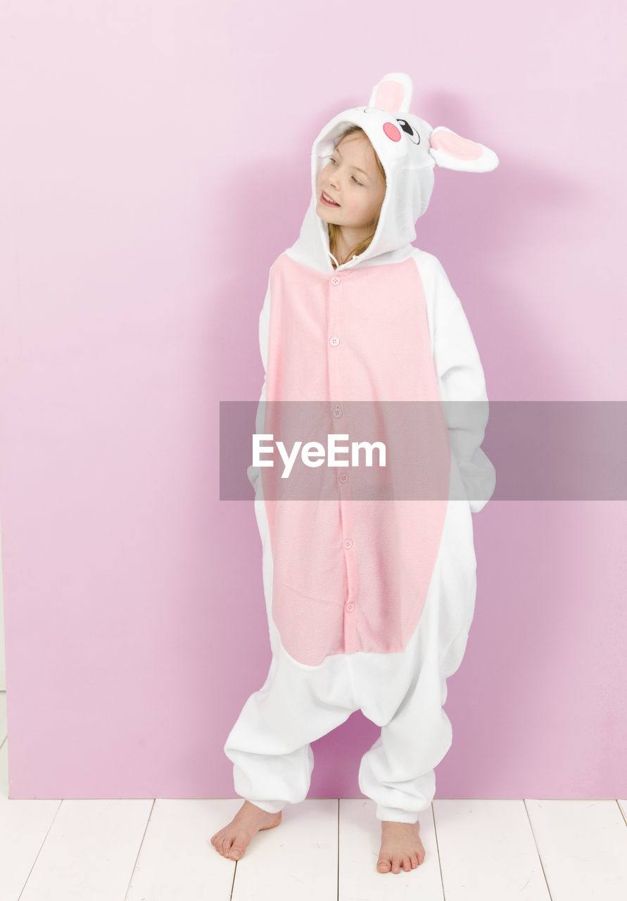 TEENAGE GIRL LOOKING AWAY WHILE STANDING AGAINST PINK WALL