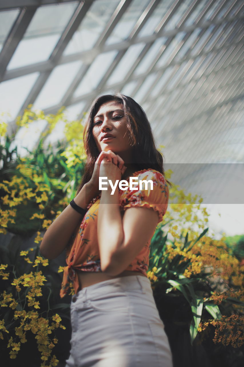 Low angle view of beautiful woman standing by flowering plants in park