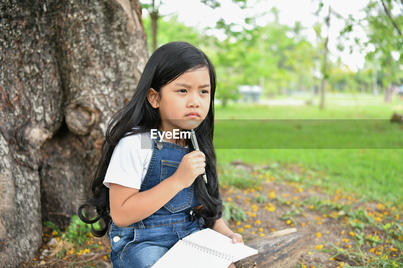 Thoughtful girl studying with sitting against tree at park