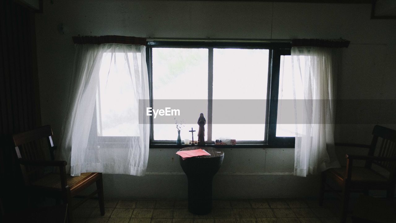 MAN STANDING ON TABLE BY WINDOW