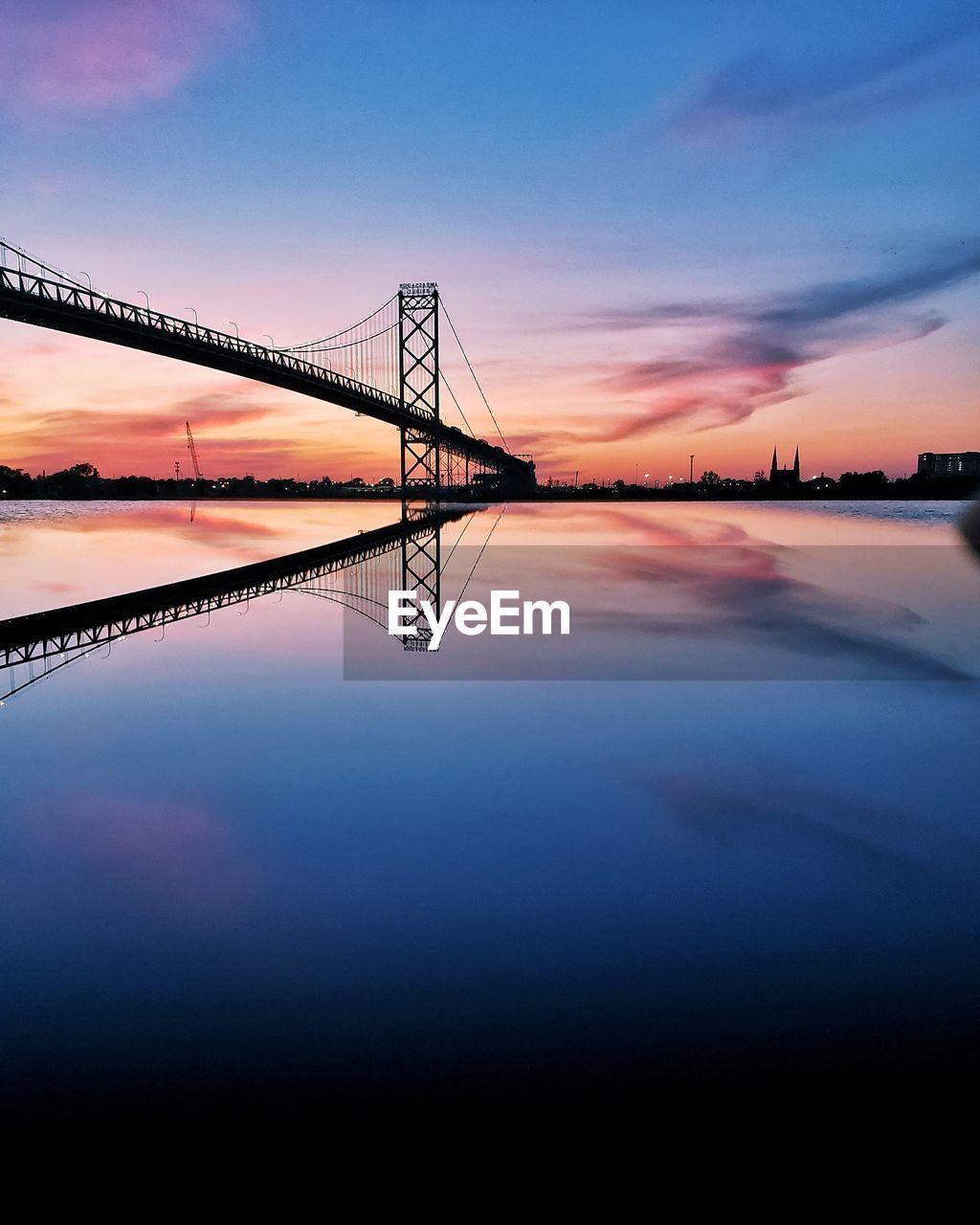 Symmetry view of silhouette bridge over river against dramatic sky during sunset