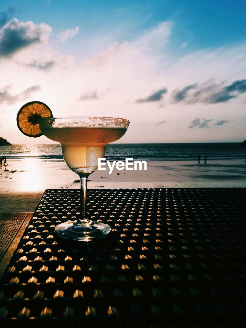 Wineglass on table by sea against sky during sunset