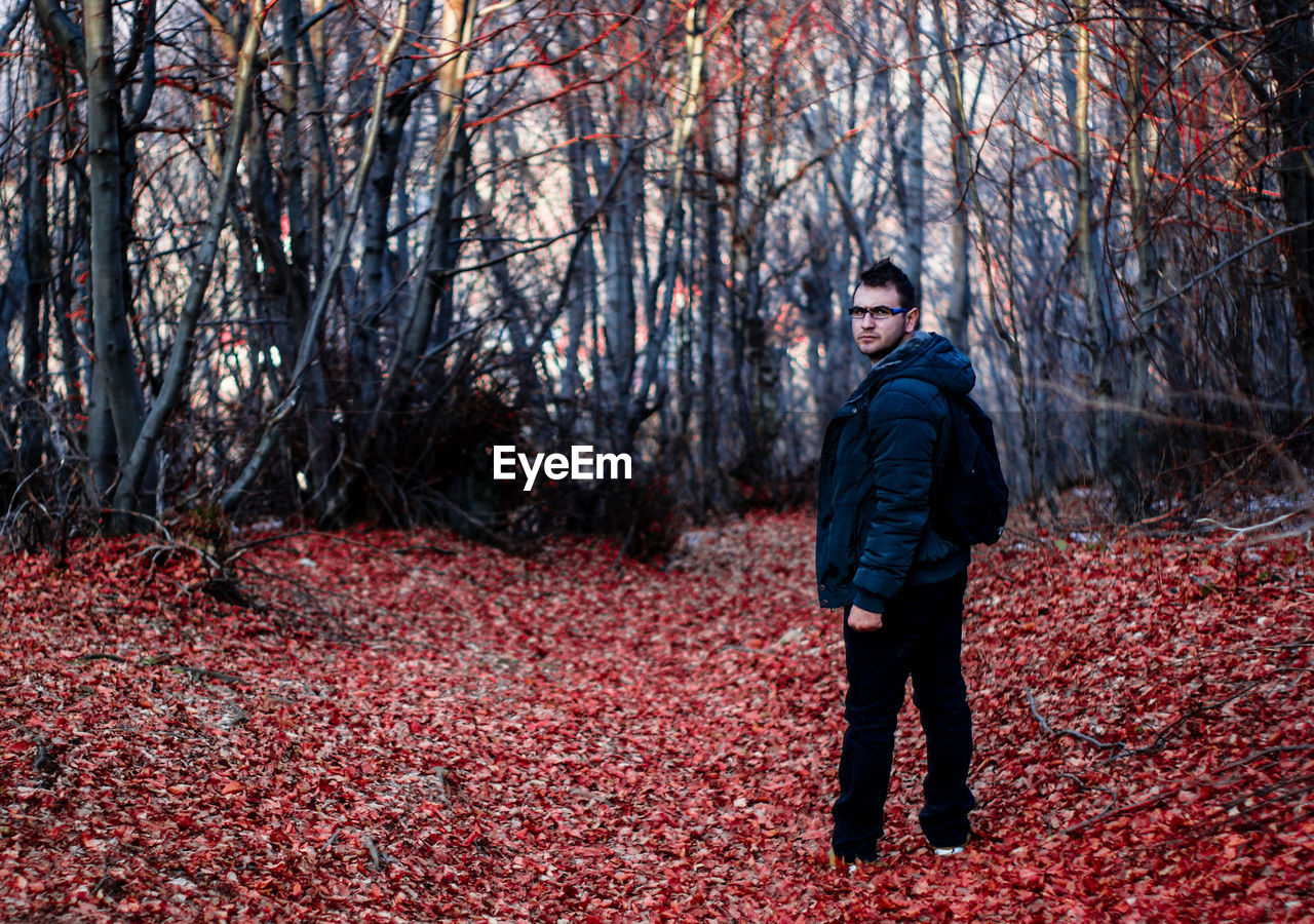 Full length of man standing on fallen leaves against trees at forest