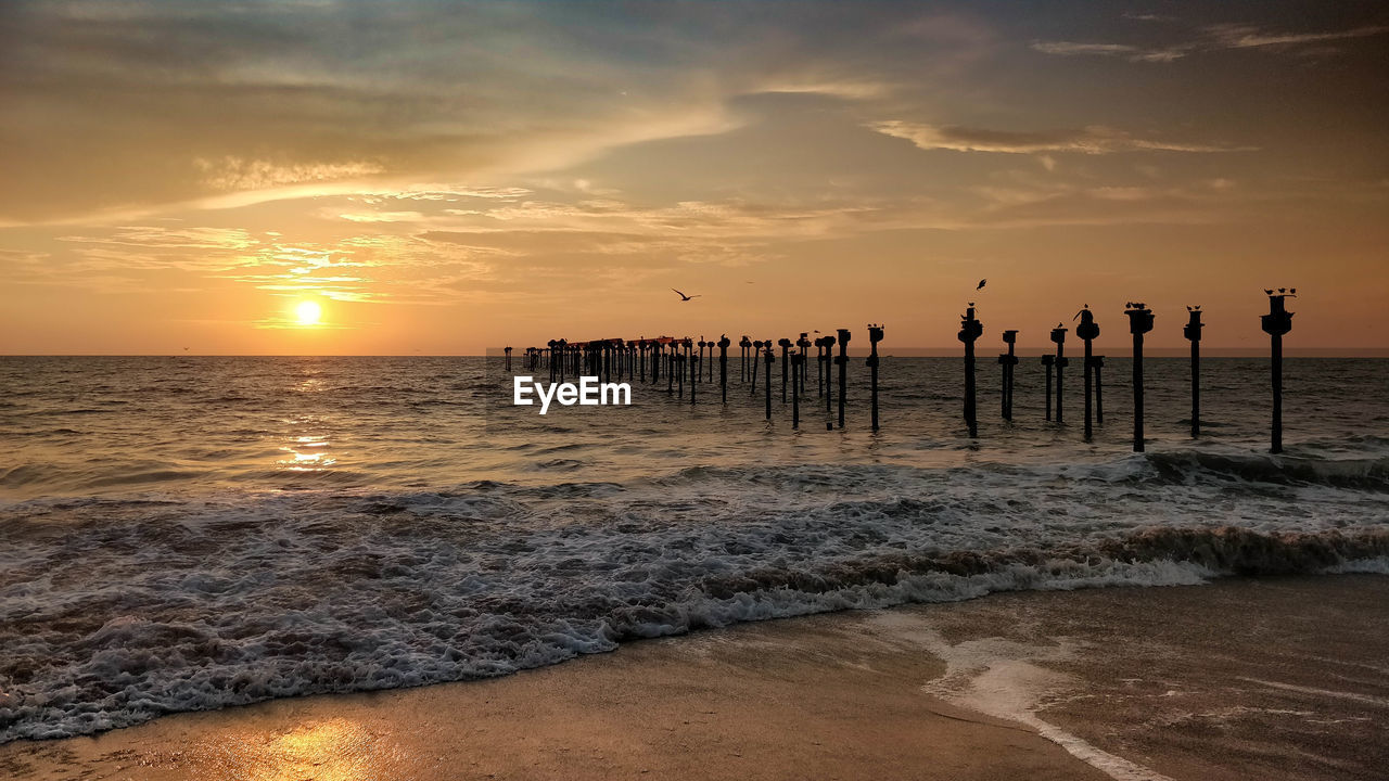   view of pier on beach against sky during sunset