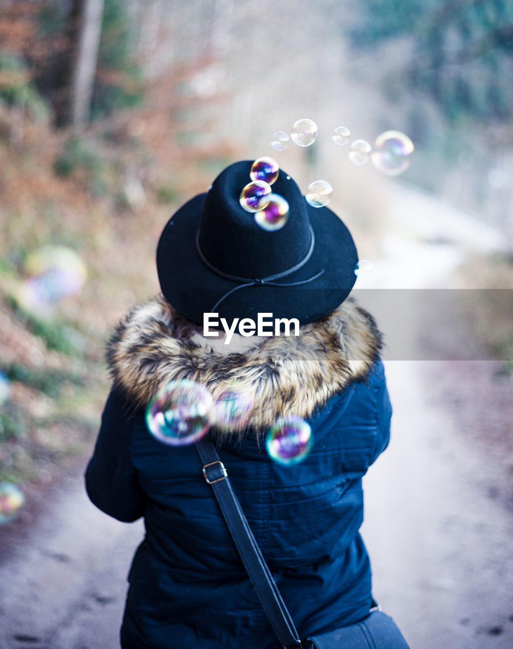 Rear view of woman wearing hat and fur coat by bubbles in mid-air