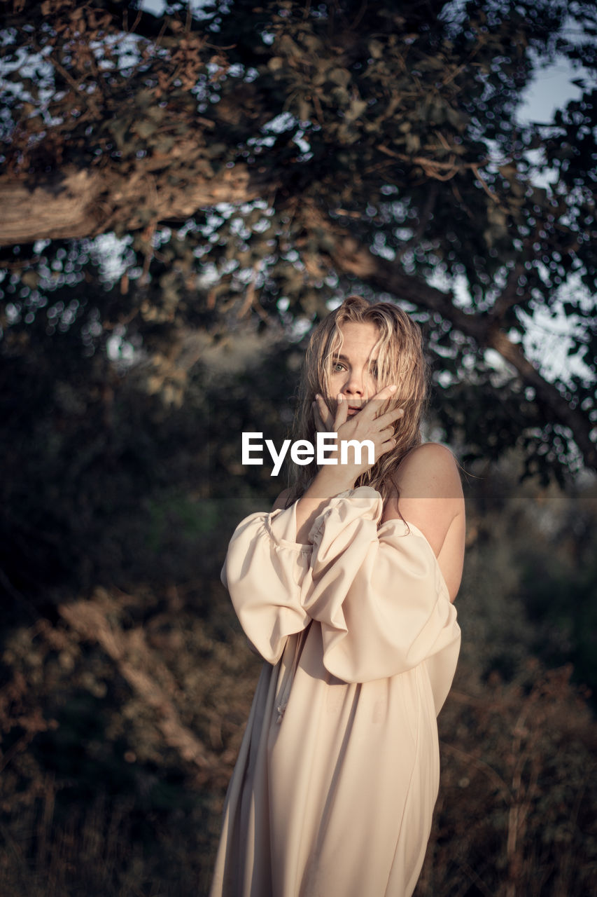 Portrait of woman posing while standing by tree in forest