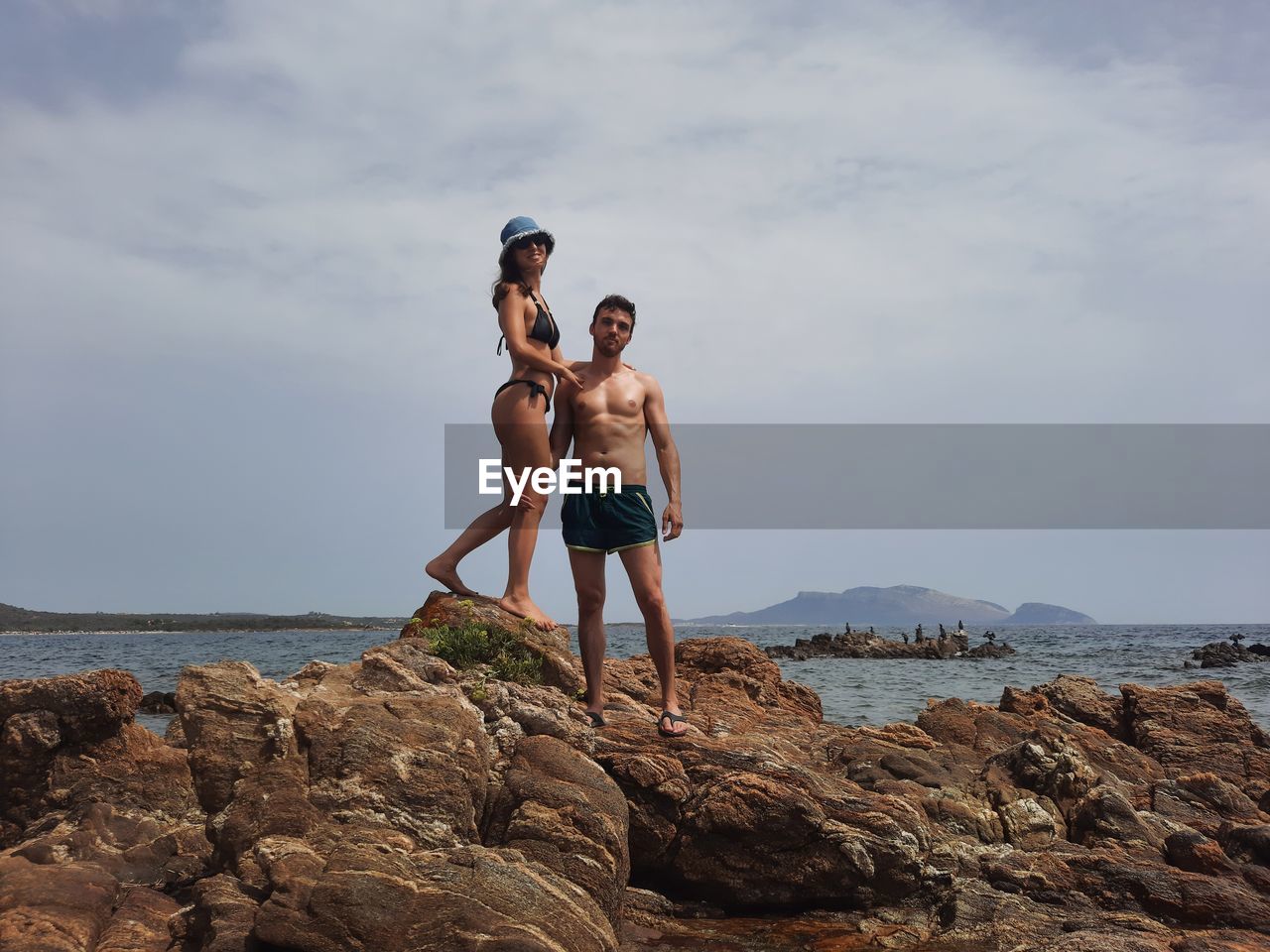 Full length of young couple standing on rock by sea against sky