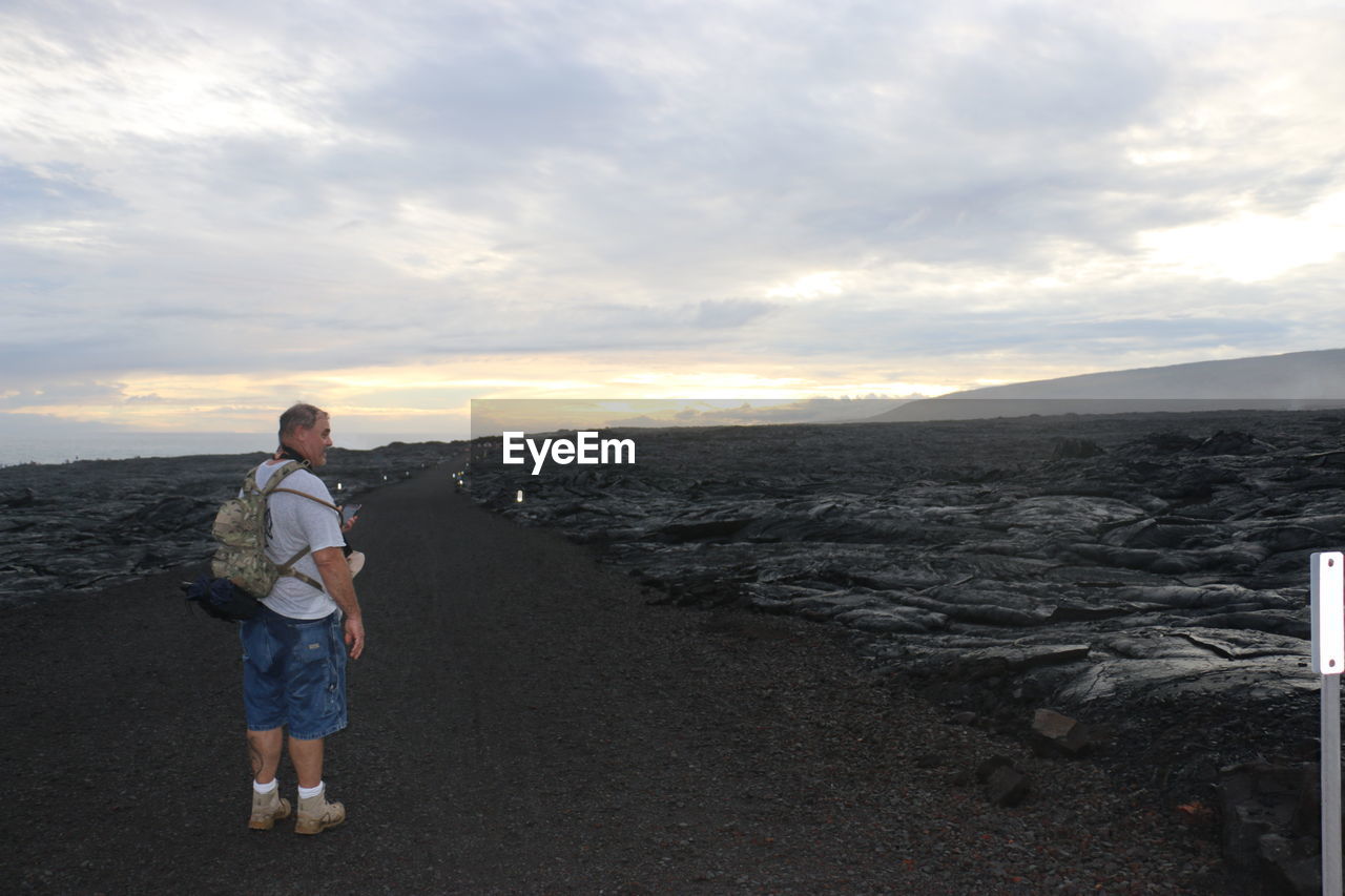 Rear view of man walking at beach against sky during sunset