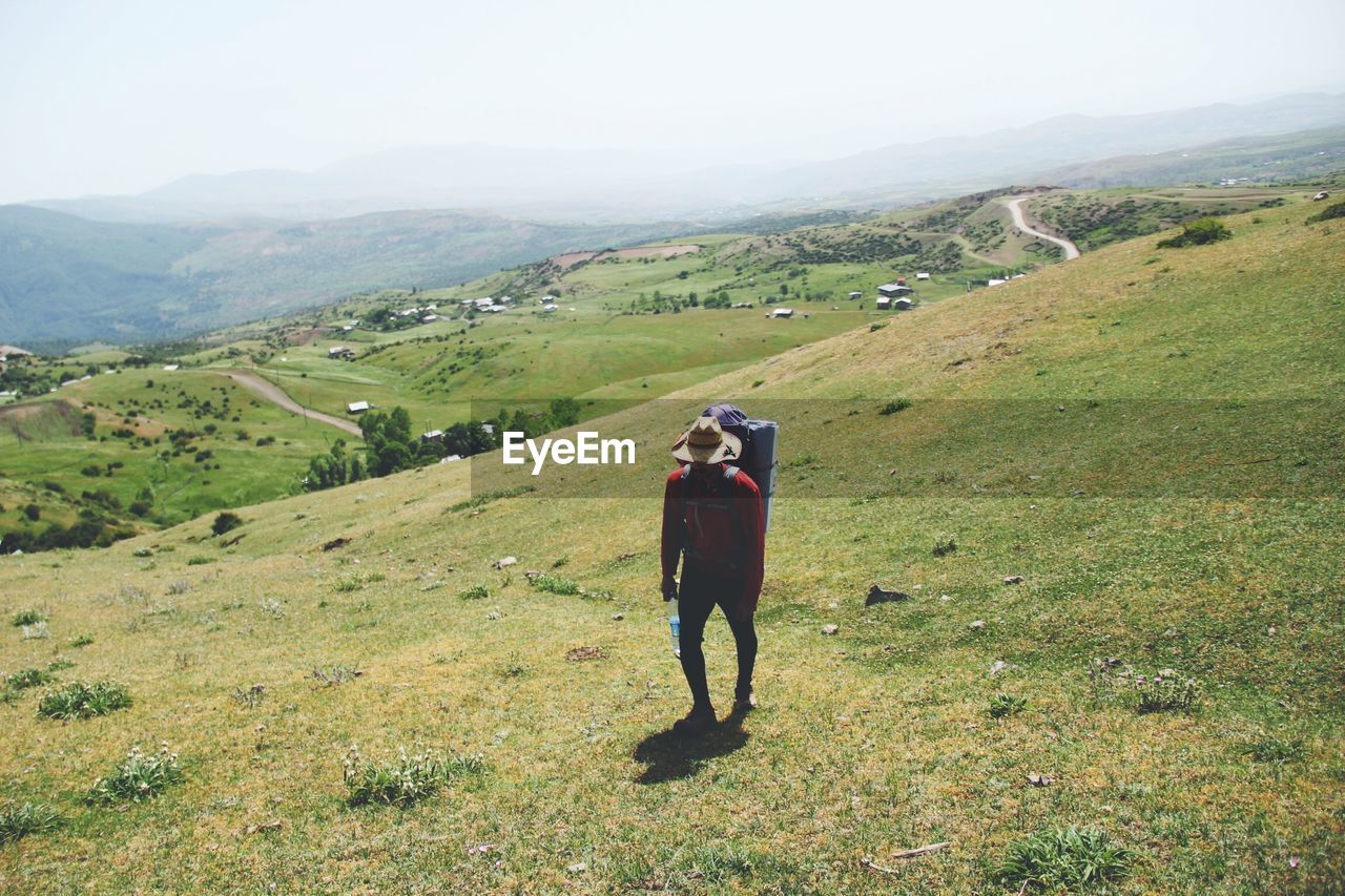 Backpack man hiking on green mountain against clear sky