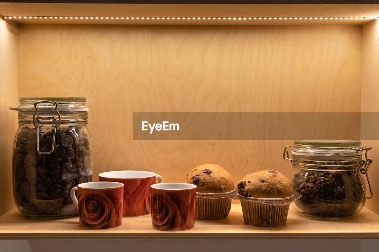 Muffins, cups of coffee and glass jars containing coffee and cocoa, breakfast theme.