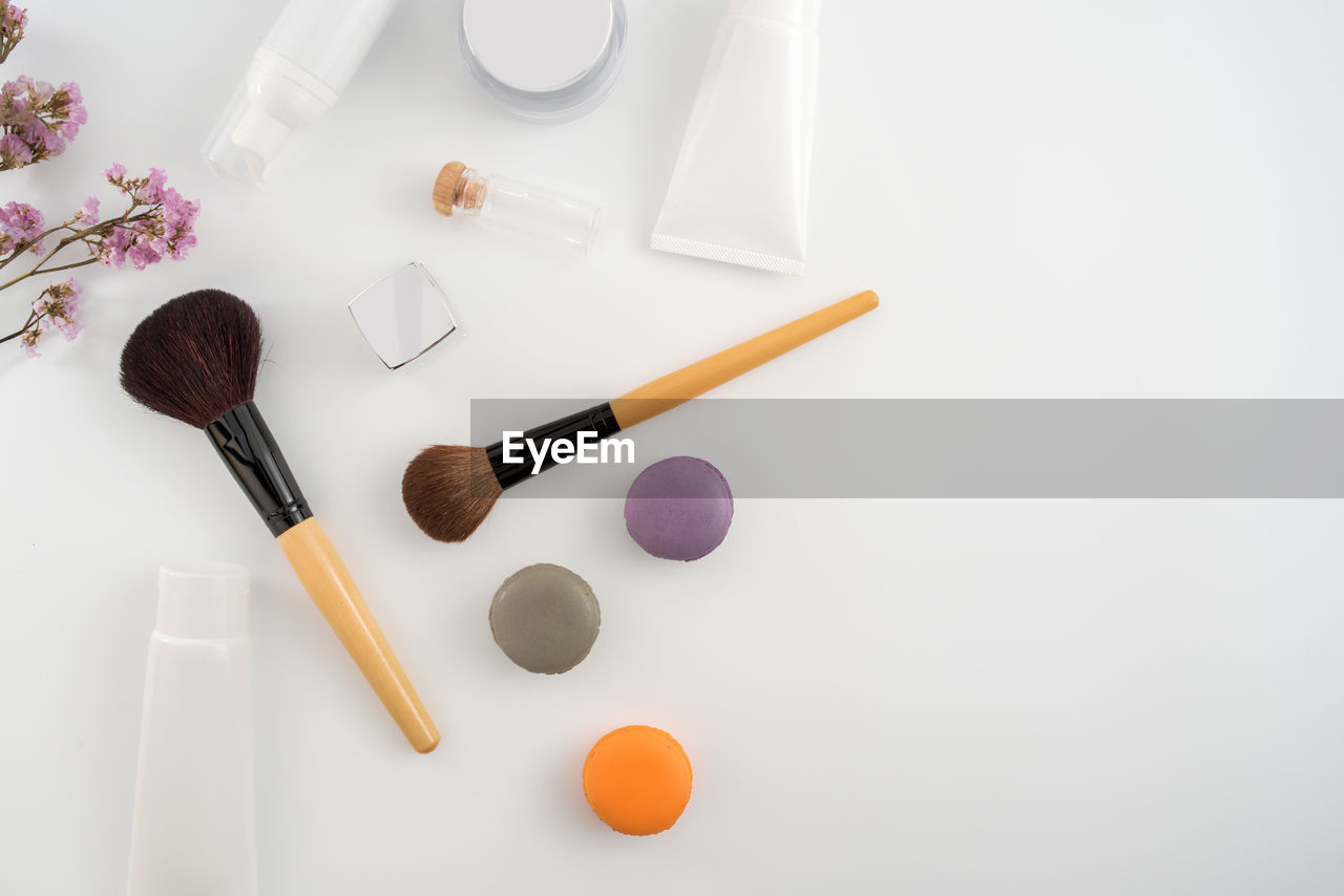 High angle view of beauty products with macaroons on white background