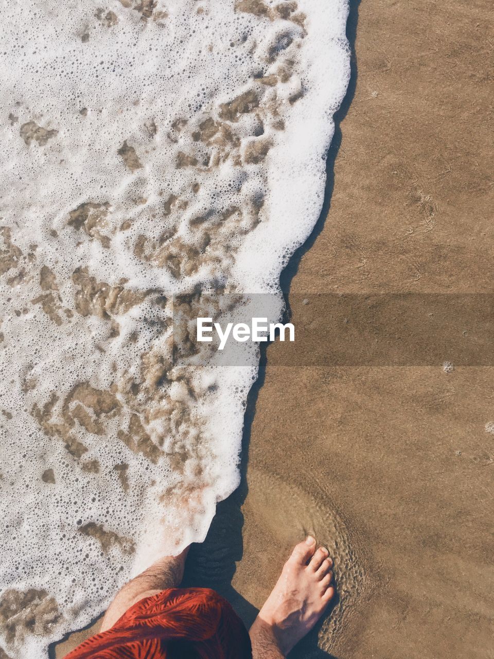 Low section of man standing on sand at beach