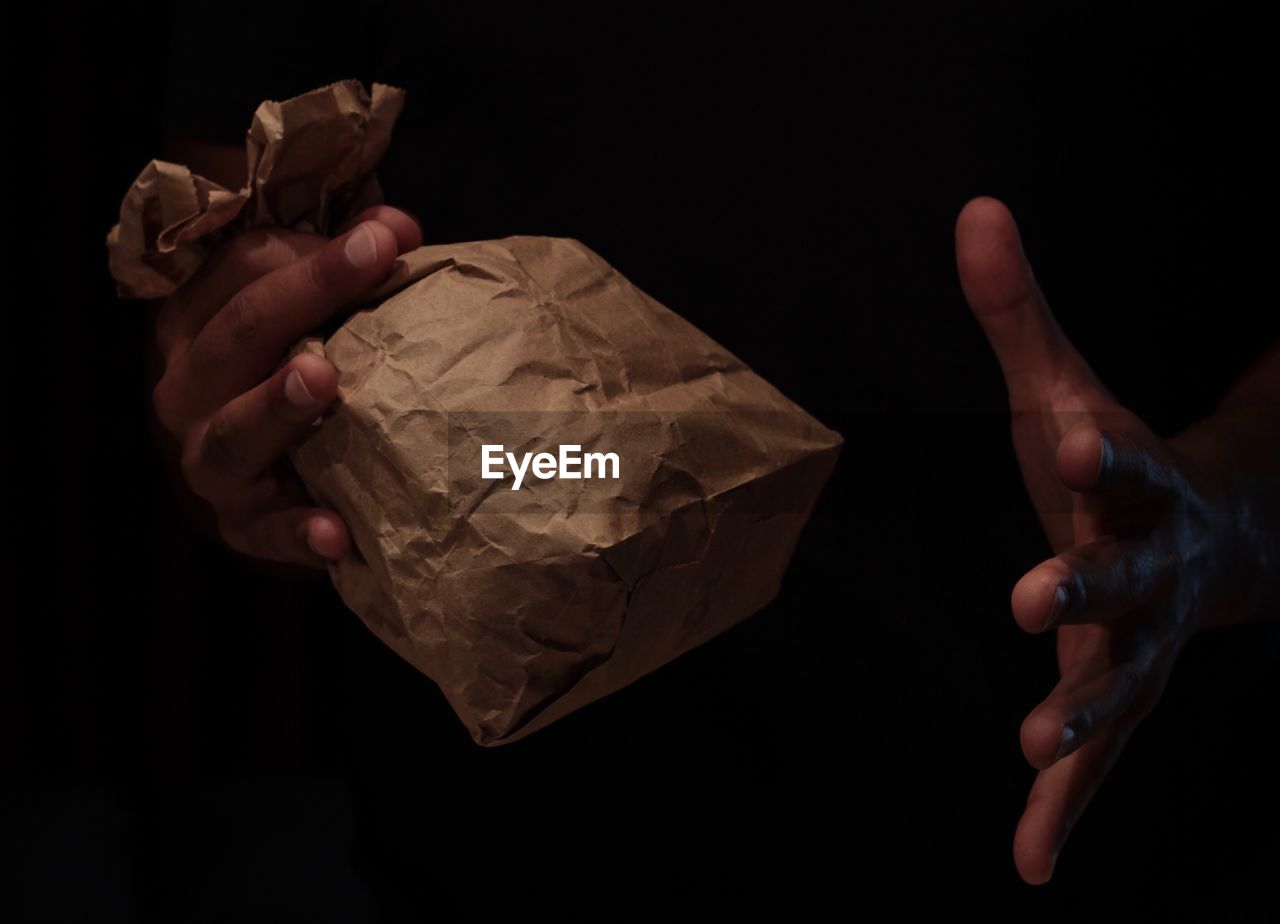 Close-up of human hand holding paper bag against black background