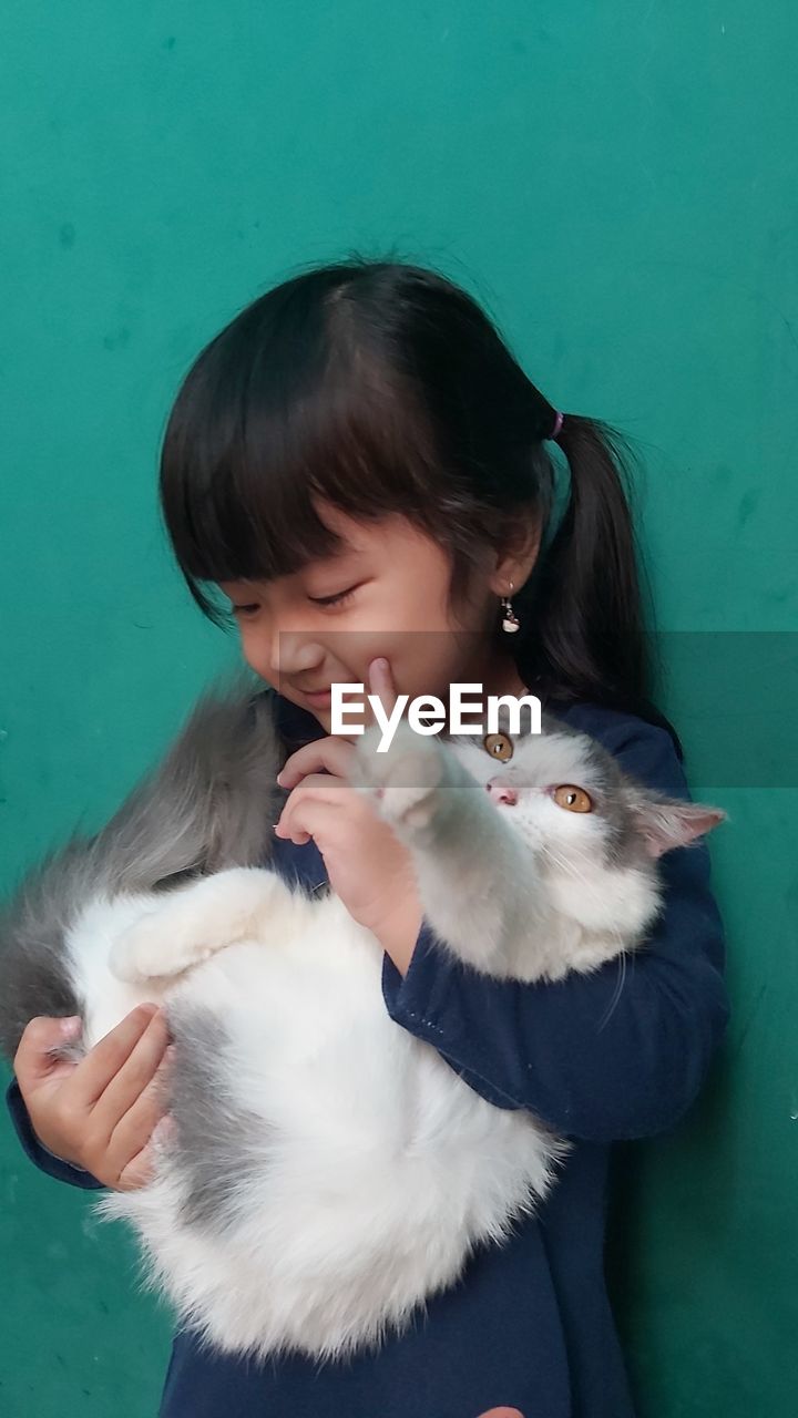 Cute girl carrying cat while standing against blue background