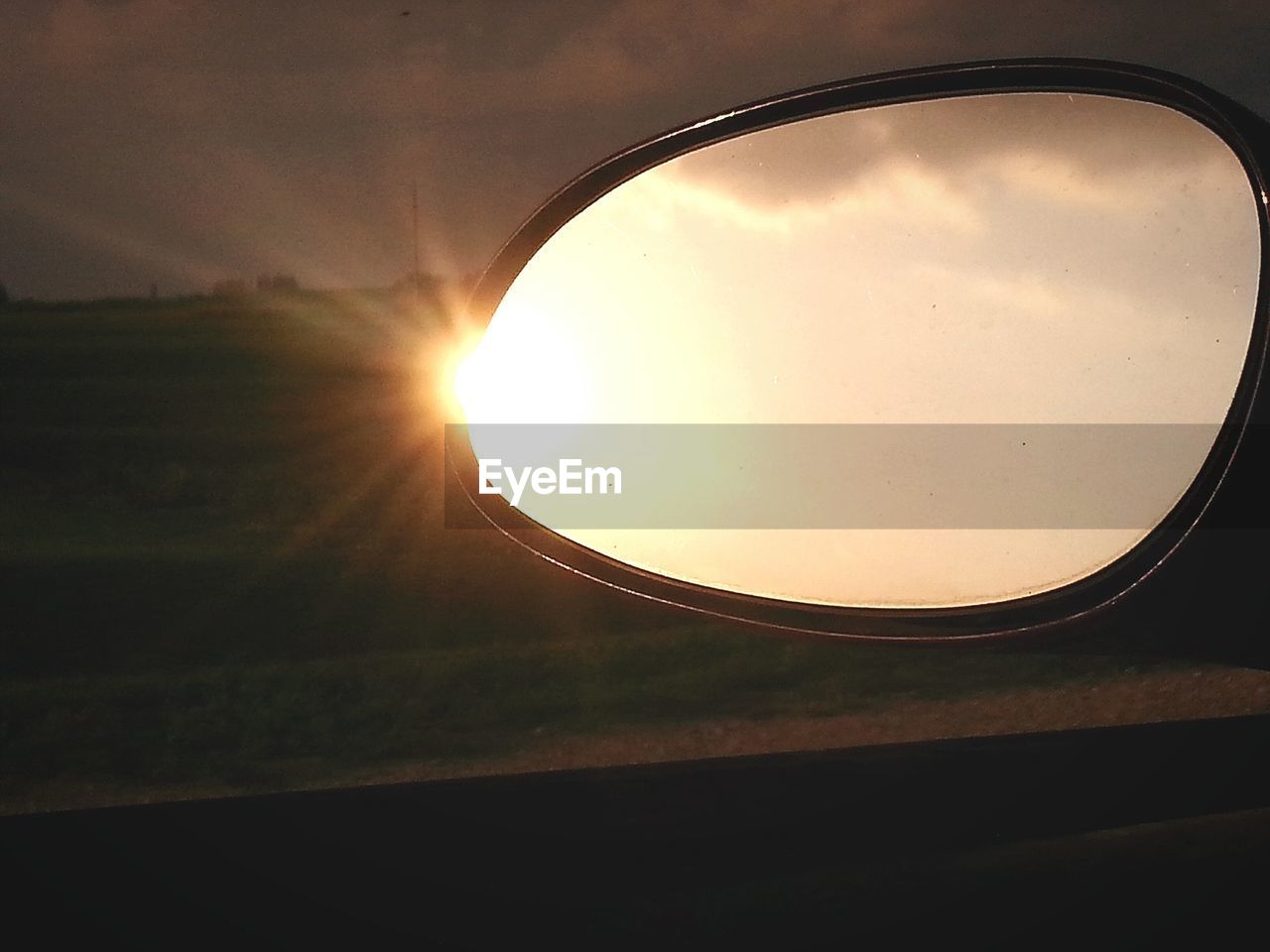 Sky reflecting on car side-view mirror during sunset