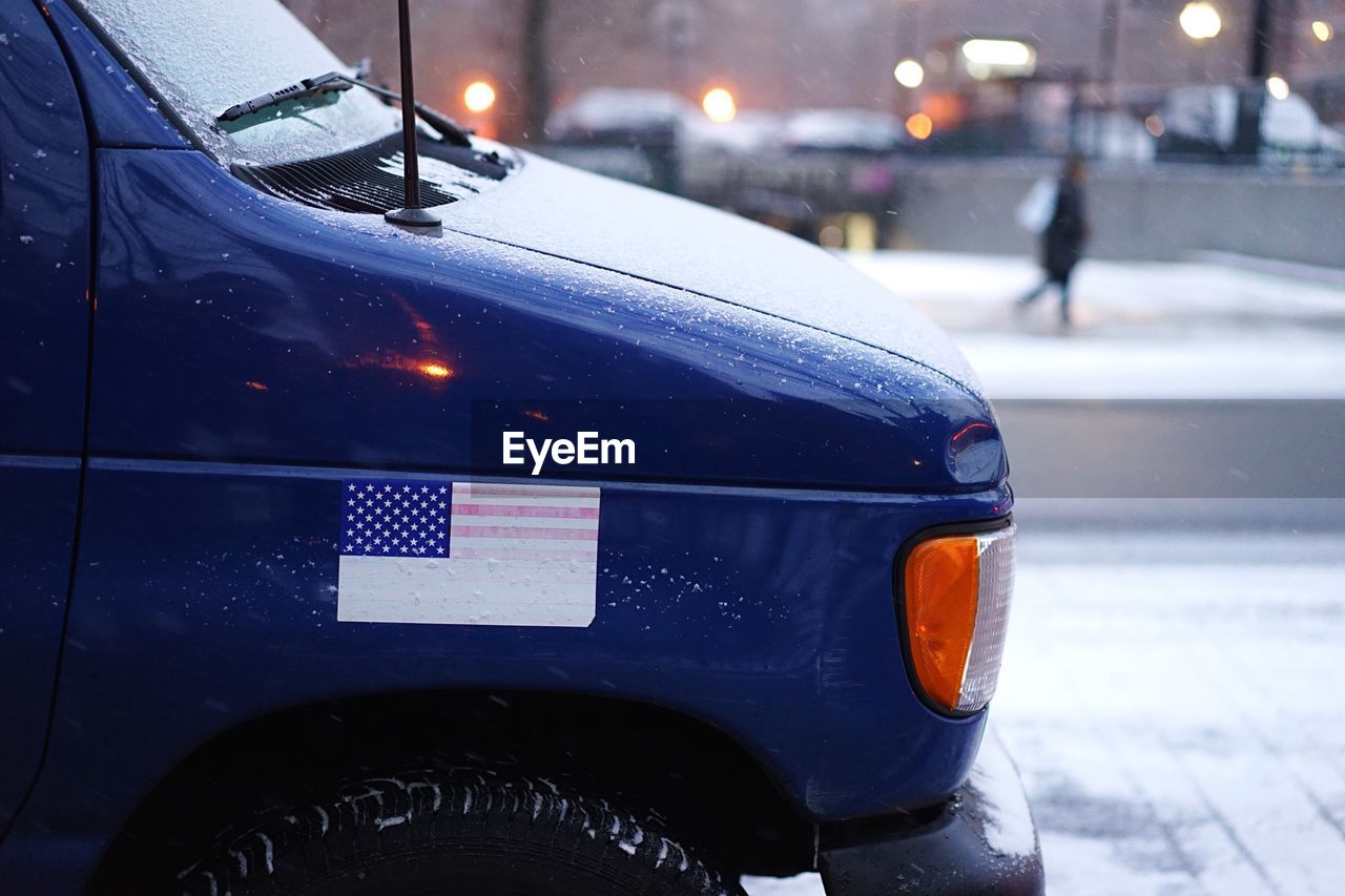 Cropped image of car with american flag on street during winter