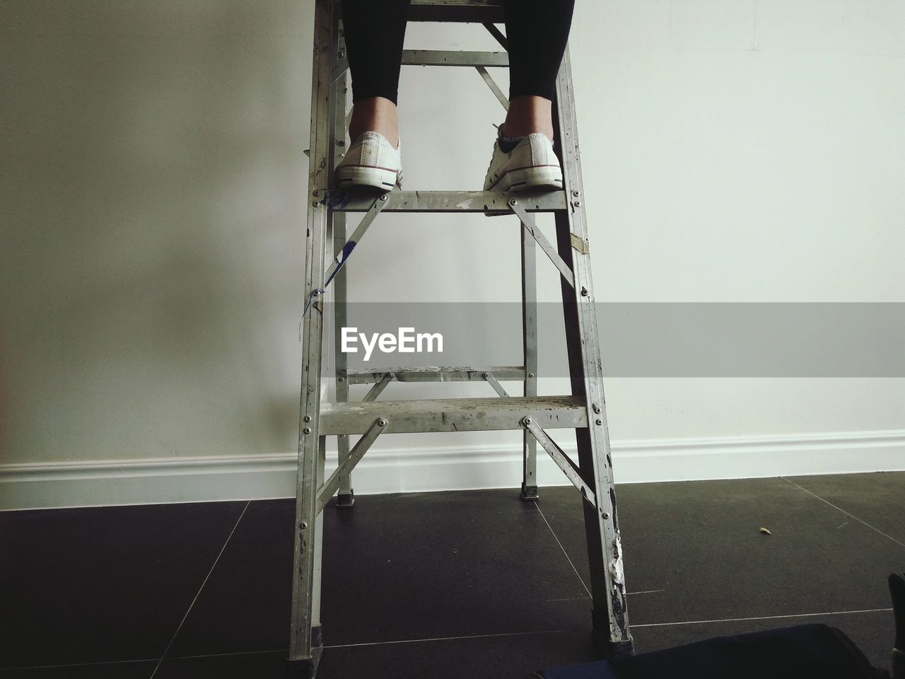 Low section of woman standing on step ladder against wall