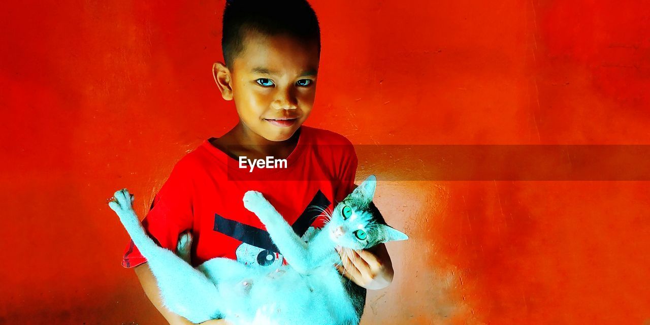 PORTRAIT OF BOY HOLDING RED ORANGE AGAINST WALL AGAINST SKY