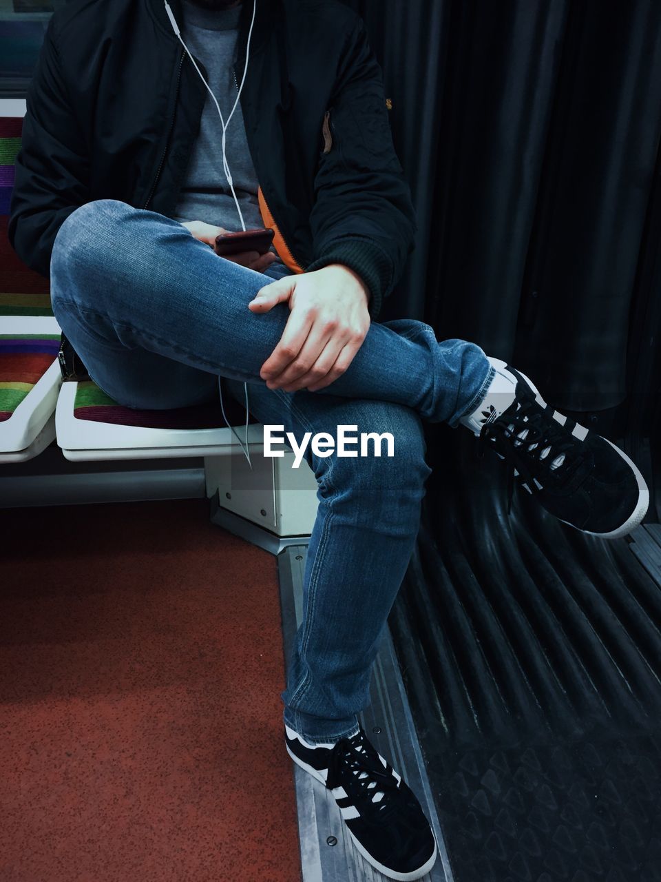 Low section of man using phone while sitting on seat