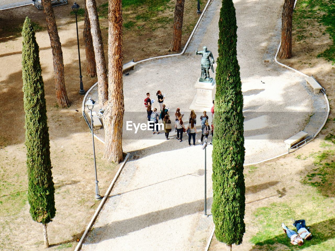 High angle view of students standing by statue on footpath in park