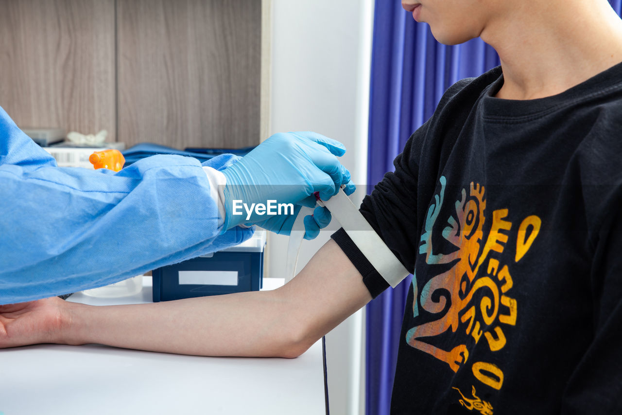 Nurse tightening the elastic band on a male patient arm to collect a blood sample from in a clinic