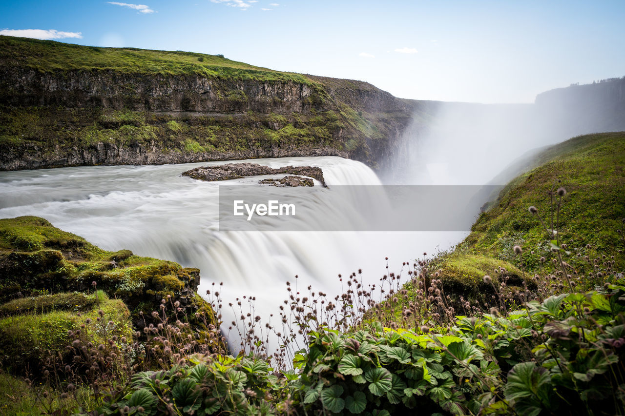 Idyllic view of waterfall by mountain against sky