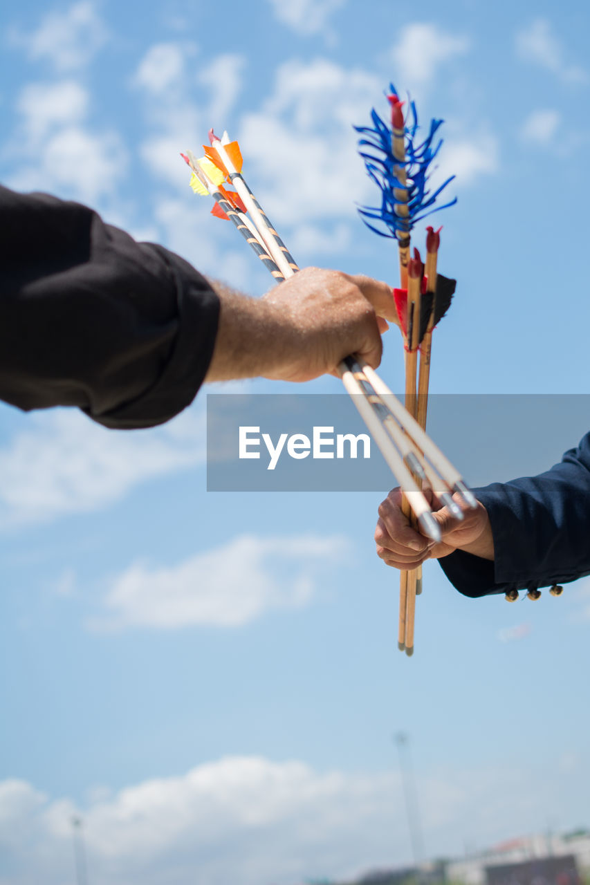 Low angle view of hands holding arrows against blue sky