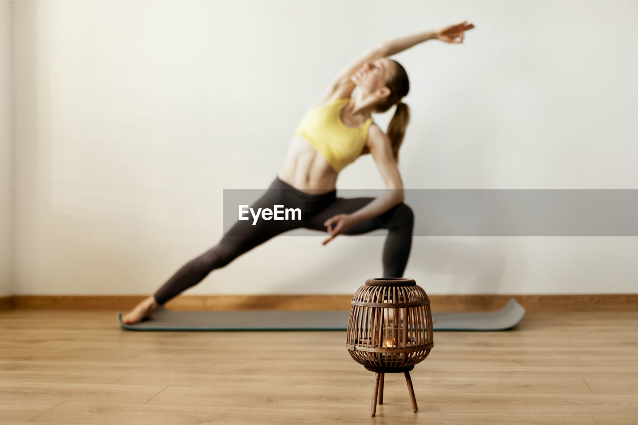 Close-up of oil lamp on floor with woman exercising in background against wall