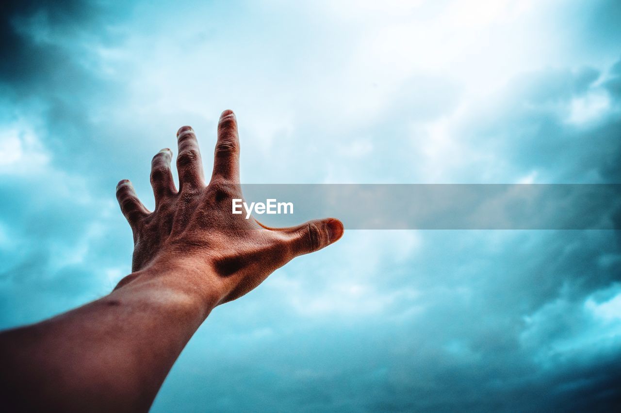 Close-up of hand against storm clouds