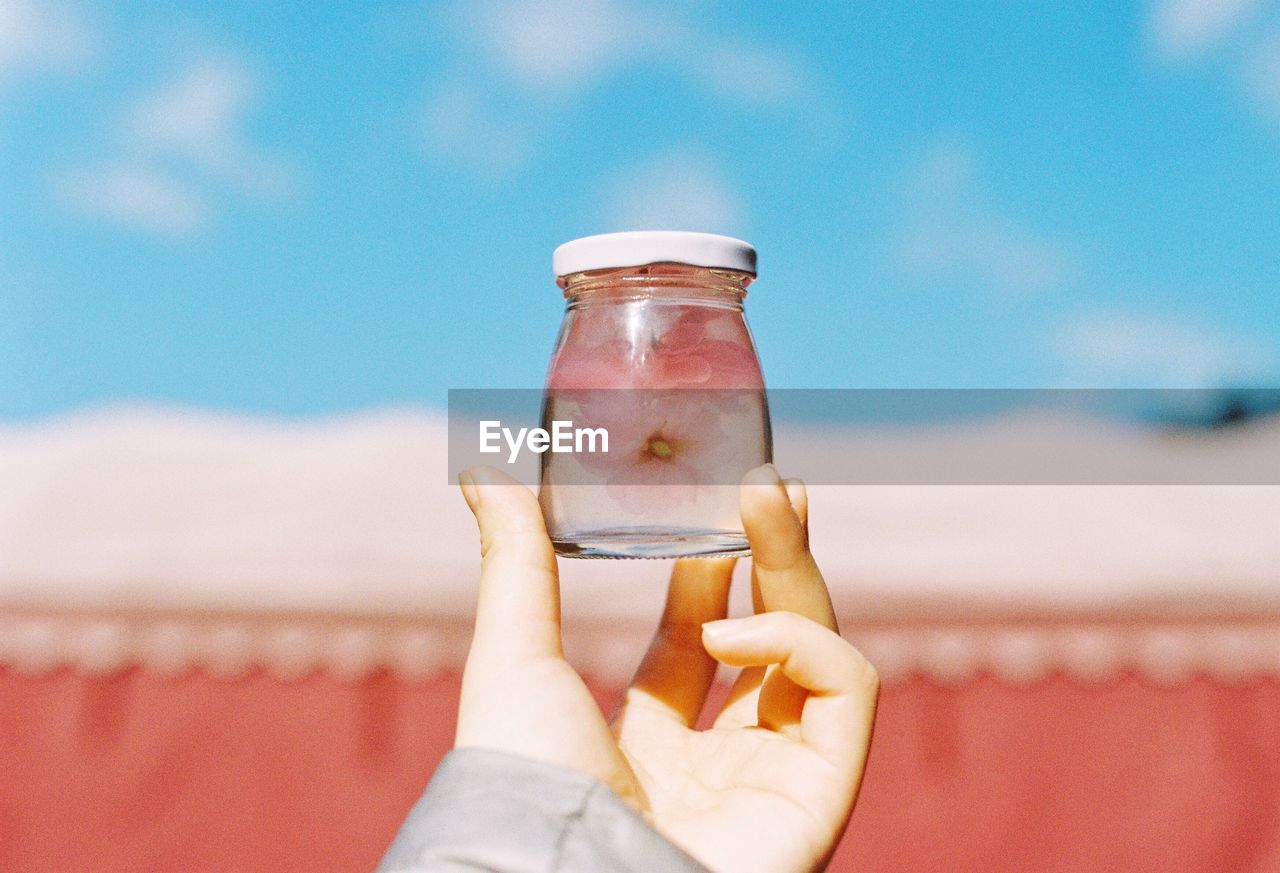 Cropped image of person holding jar against sky
