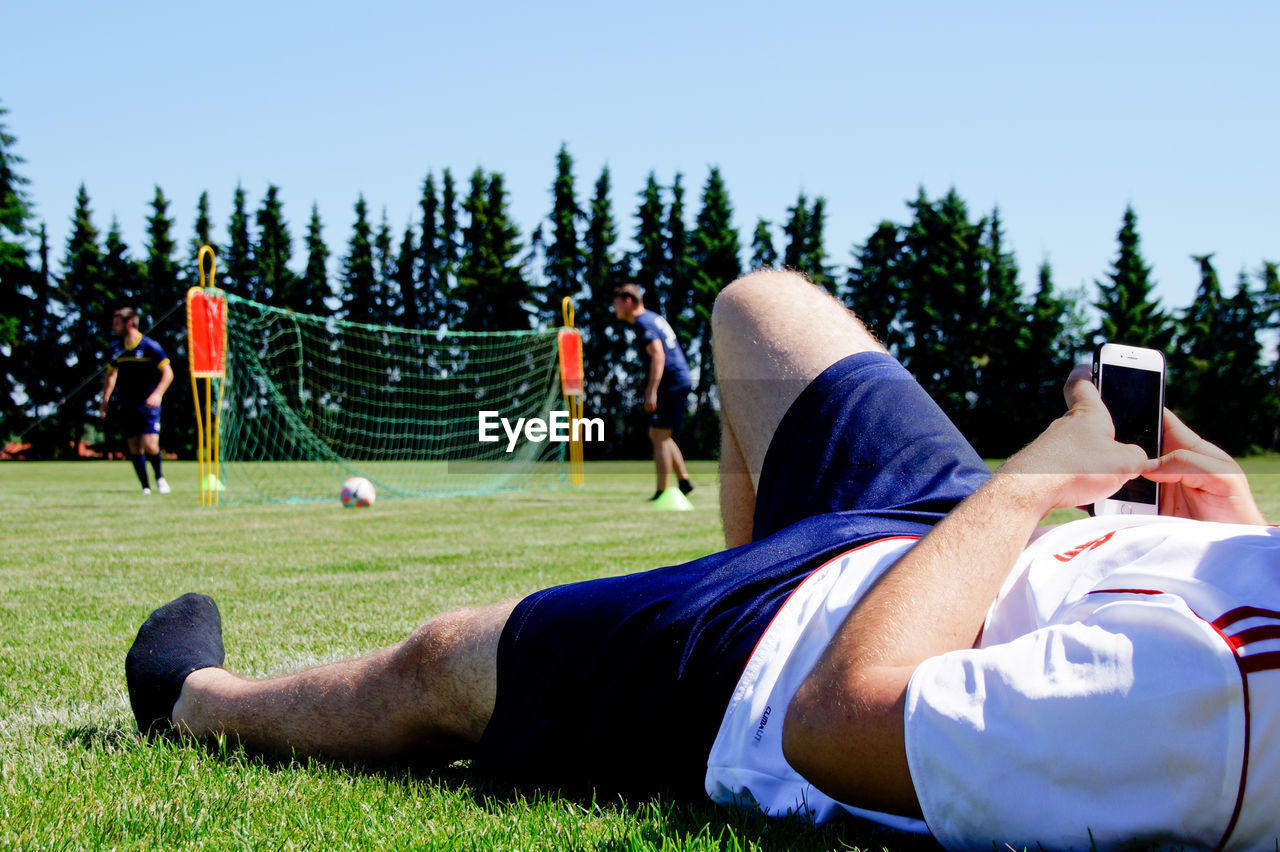 Close-up of man using mobile phone while lying on soccer field