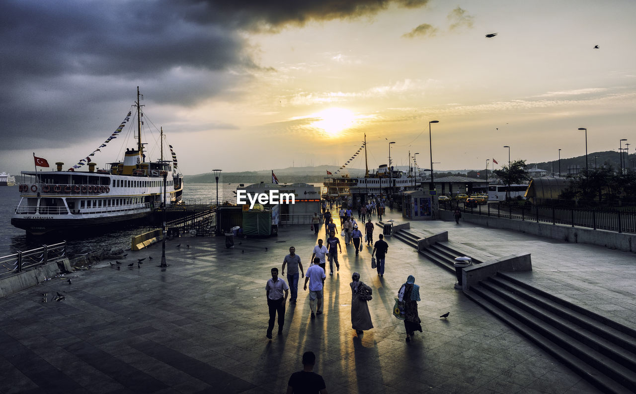 People at harbor against sky during sunset