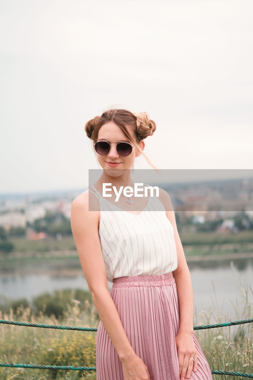 Portrait of young woman wearing sunglasses standing against clear sky